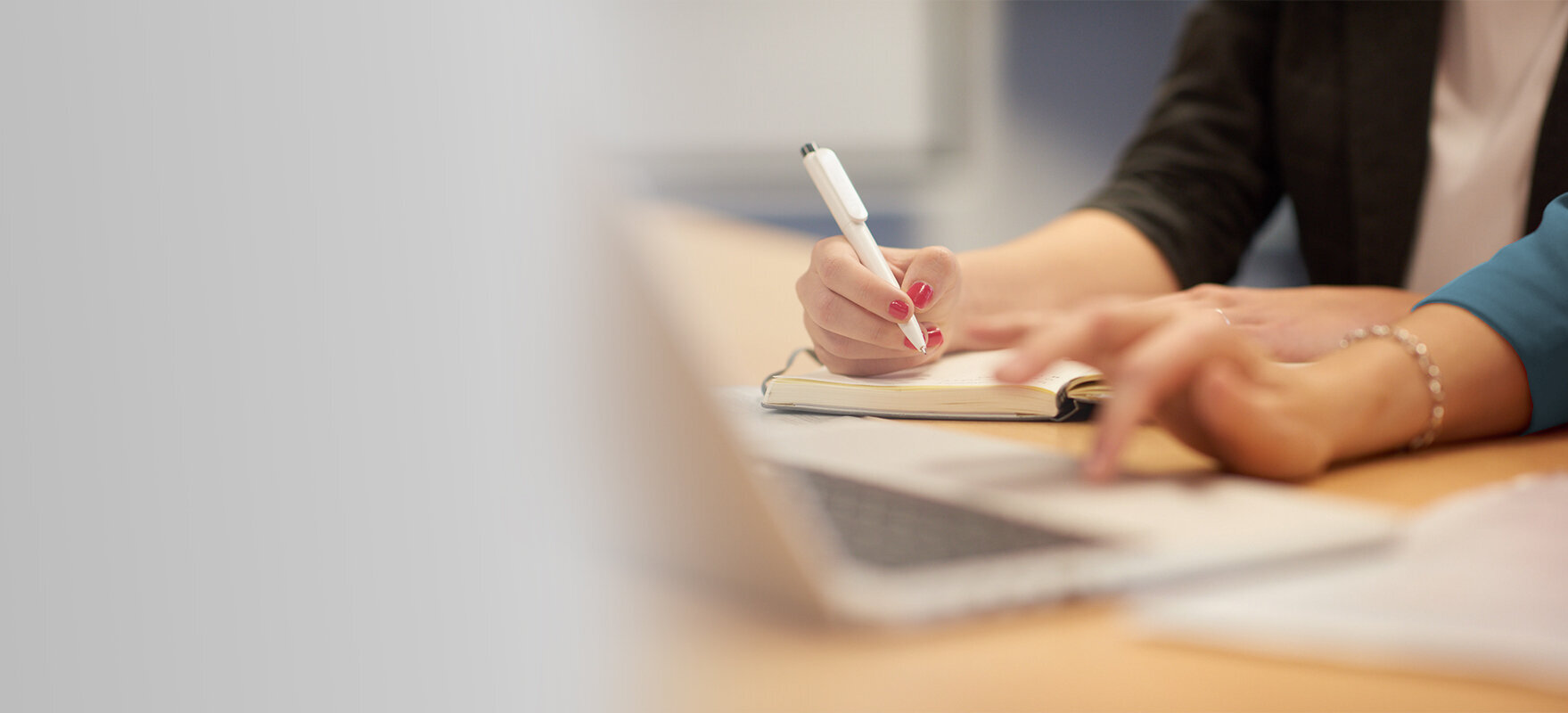 Two people working together at a desk, writing notes and using a laptop.