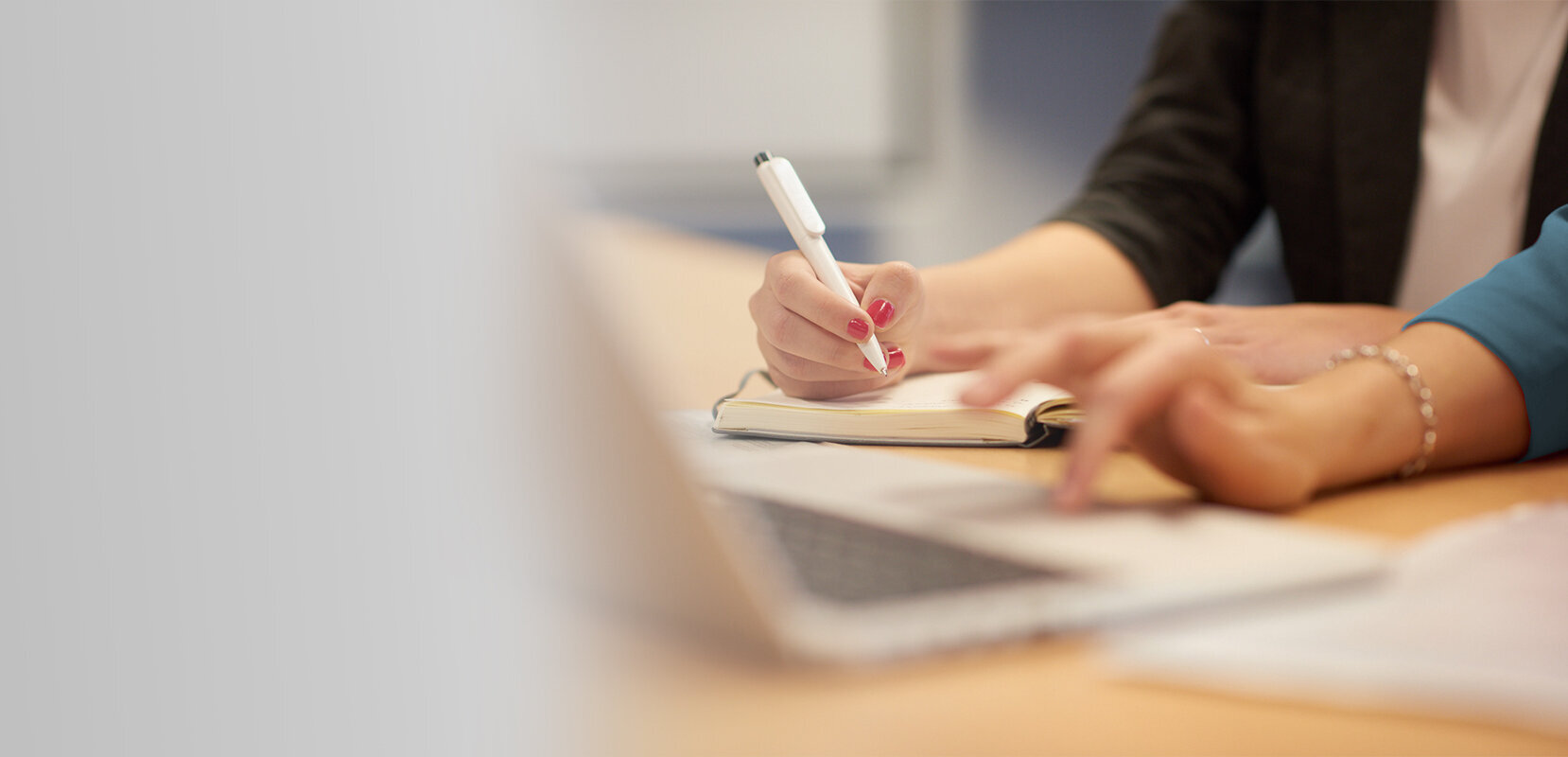 Two people working together at a desk, writing notes and using a laptop.