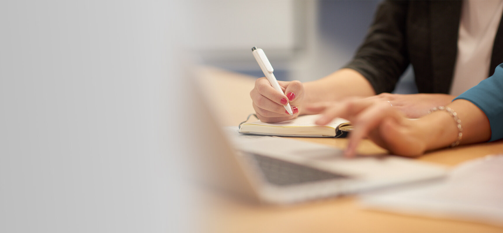 Two people working together at a desk, writing notes and using a laptop.